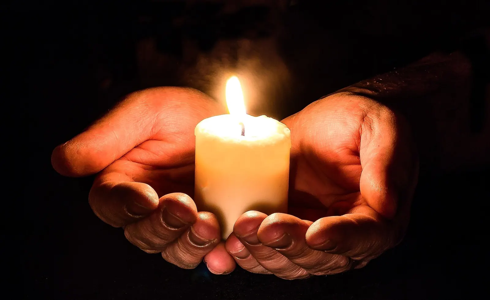 Manos sosteniendo una vela encendida en la oscuridad, símbolo de la Capilla Virtual